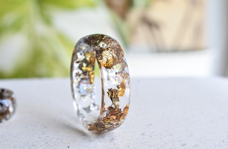 K&ouml;nnte beinhalten: Ein klarer Harzring mit eingebettetem Blattgold. Der Ring ist dick und hat eine abgerundete Form.