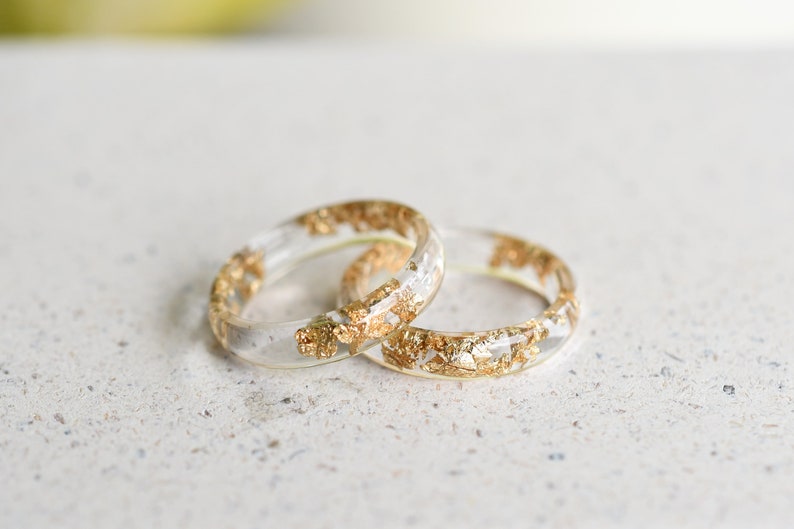 May include: Two clear resin rings with gold flakes embedded inside. The rings are stacked on top of each other.