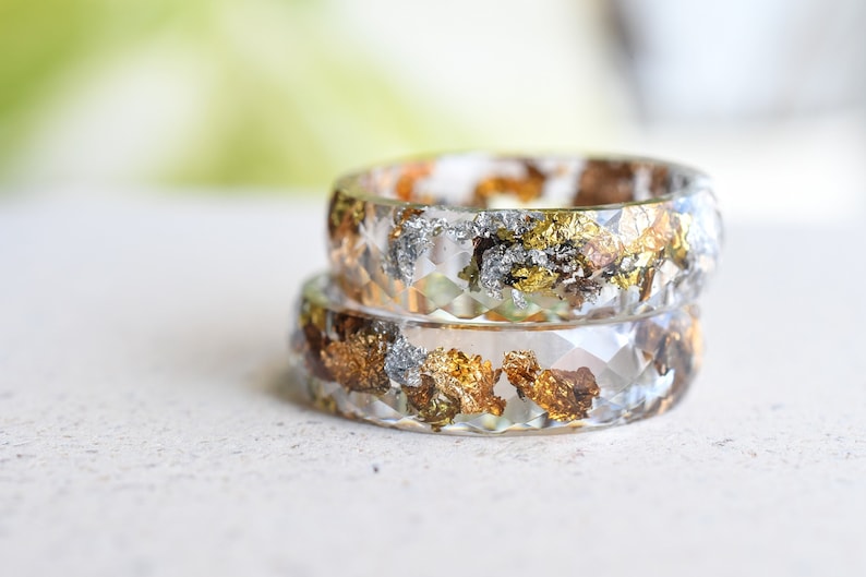 K&ouml;nnte beinhalten: Zwei transparente Harzringe mit eingebetteten Gold- und Silberbl&auml;ttern. Die Ringe sind &uuml;bereinander gestapelt.