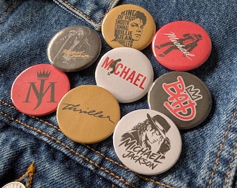 May include: A collection of nine circular pin-back buttons featuring Michael Jackson imagery and text. Designs include the text King of Pop, Smooth Criminal, Billie Jean, Thriller, Bad, and MJ, alongside silhouettes and portraits of the artist in various colors.