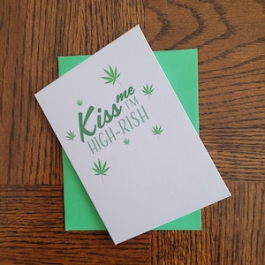 May include: A white card with green marijuana leaf illustrations and the text "Kiss me I'm high-rish".