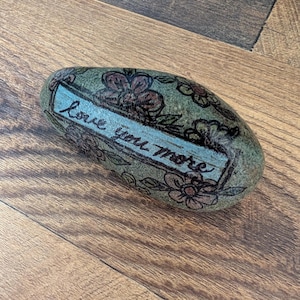 Hand-Painted Rock – “Love You More” Light Blue Banner with Colorful Flowers | 3.75&quot;x2&quot; Decorative Paperweight, Gift, Rock Art