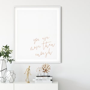 May include: A white framed print with the text "you are more than enough" written in a cursive font in brown ink.