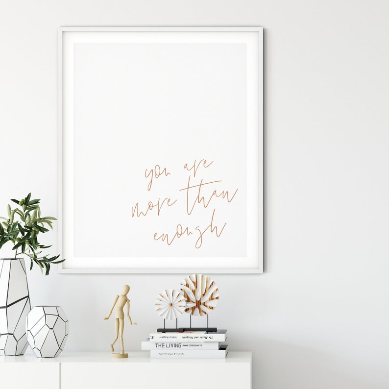 May include: A white framed print with the text "you are more than enough" written in a cursive font in brown ink.
