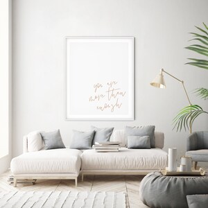 May include: A white framed print with the text "you are more than enough" in brown script on a white background. The print is hanging on a white wall above a white couch with gray pillows.