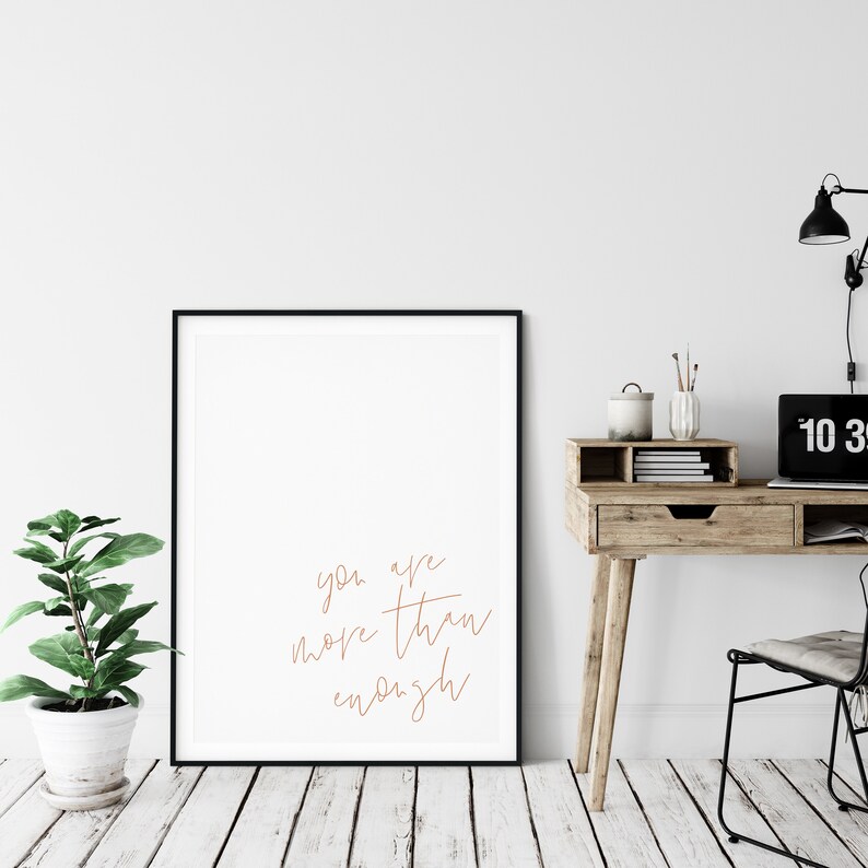 May include: A black framed poster with a white background and the text "you are more than enough" written in a cursive font in a light brown color.
