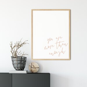 May include: A framed print with a white background and the text "you are more than enough" written in brown cursive script.