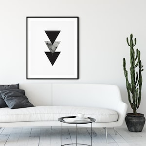 May include: A black and white geometric print with three triangles in a descending pattern. The print is framed in a black frame and is hanging on a white wall above a white couch.