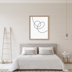 May include: A white bed with a white duvet cover and two gray pillows. A wooden ladder leans against the wall behind the bed. A framed black and white line art print hangs above the bed.