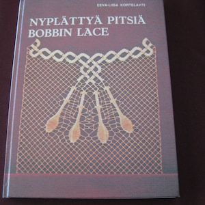 May include: A book titled "NYPLÄTTYÄ PITSIÄ BOBBIN LACE" with a close-up image of a delicate, intricate bobbin lace pattern in cream on a purple background.