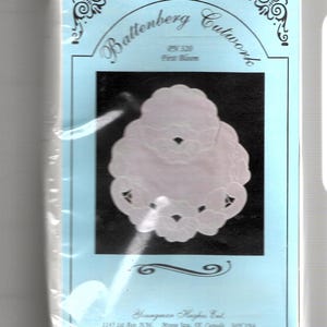 May include: A white Battenberg Cutwork pattern with a floral design. The pattern is on a light blue background with the text "Battenberg Cutwork" and "PN 320" printed on it.