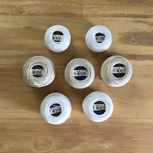 May include: Six spools of white embroidery floss with blue labels. The labels have the text "BLANC N° 8", "BLANC N° 24", "ECRU N° 40", "ECRU N° 50", "BLANC N° 8", and "BLANC N° 8".
