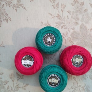 May include: Four spools of thread, two green and two red. The spools are labeled "ALTIN BASAK" and have a number on each spool. The green spools are labeled "RENKLİ DANTEL İPLİĞİ" and the red spools are labeled "MPL 233".