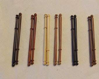 May include: A selection of wooden lace bobbins in shades of brown, tan, and black. Each bobbin features a rounded top and bottom with a decorative ring. The bobbins are arranged in pairs, showcasing their varied colours.