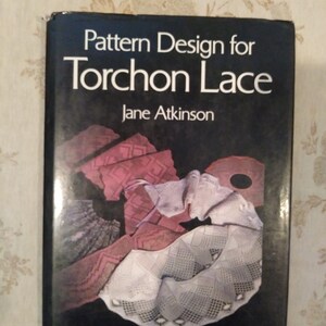 May include: A black book with the title "Pattern Design for Torchon Lace" by Jane Atkinson. The cover features a close-up of white and red lace.