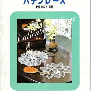 May include: A book cover with Japanese text and the title "Batten Lace." The cover features a teal border and a dark wooden table with white lace doilies, a small wooden jewelry box, and a vase of flowers. A gold-colored hand fan is also visible.