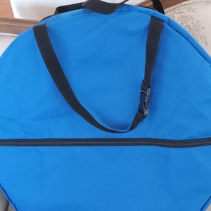 May include: A blue round zippered bag with a black adjustable strap and buckle. The bag is made of a durable fabric and has a zipper closure.