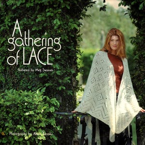 May include: A woman wearing a cream-colored, open-weave shawl with a geometric pattern. The shawl is draped over her shoulders. The image includes the text "A gathering of LACE" and "Gathered by Meg Swansen".