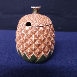 May include: A ceramic pineapple-shaped sugar bowl with a lid. The bowl is brown and green with a textured surface.