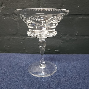 May include: A clear glass stemmed cocktail glass with a cut crystal design. The glass has a wide bowl and a tall, slender stem.