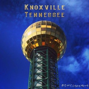 Puede incluir: Una esfera dorada y espejada en la cima de una torre de metal verde contra un cielo azul con nubes blancas. El texto "KNOXVILLE TENNESSEE" está en la parte superior de la imagen. El hashtag "#SeeCinnaMoon" está en la parte inferior de la imagen.