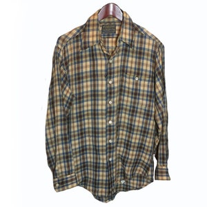 以下が含まれることがあります： 茶色、青、黄色の格子柄の長袖シャツ。シャツはボタンダウンカラーで、胸にポケットが1つ付いています。