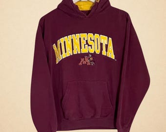 May include: Maroon hoodie with a yellow "MINNESOTA" arched text across the chest. The hoodie has a kangaroo pocket and a yellow-lined hood. A small logo is below the text. The hoodie is a vintage style.