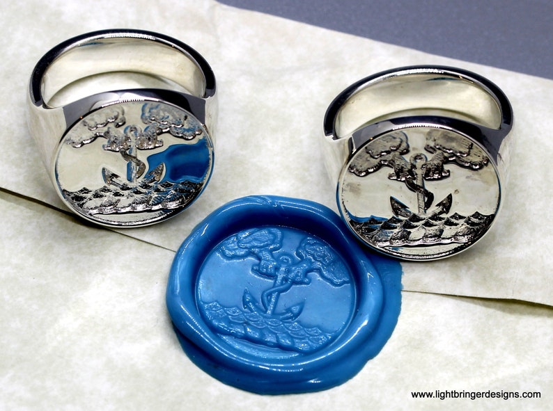 May include: Two silver signet rings with an anchor and two trees design. The rings are shown next to a blue wax seal with the same design.