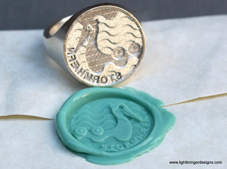May include: A silver ring with a pelican design and the words "Stormbringer" engraved on the side. The ring is used to create a wax seal with a teal blue wax impression.
