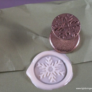 May include: A white wax seal with a snowflake design on a green envelope. A bronze snowflake stamp is next to the wax seal.