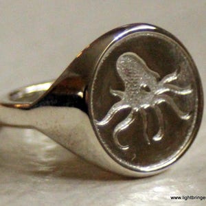 May include: A silver ring with an octopus design engraved on the top. The octopus is detailed and has a textured surface.