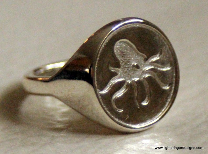 May include: A silver ring with an octopus design engraved on the top. The octopus is detailed and has a textured surface.