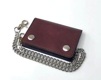 May include: A dark burgundy leather bifold wallet featuring two silver-toned metal snap closures on the front flap. A long, heavy-duty silver-colored metal chain is attached to the side of the wallet with a swivel lobster clasp hook.