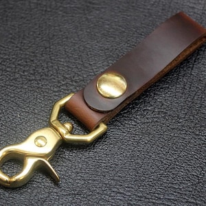 May include: A brown leather key chain with a brass hook and a brass ring. The key chain is made of high-quality leather and is durable.