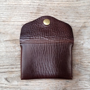 May include: A brown leather wallet with a gold button closure. The wallet has a textured surface and a flap that folds over the front.