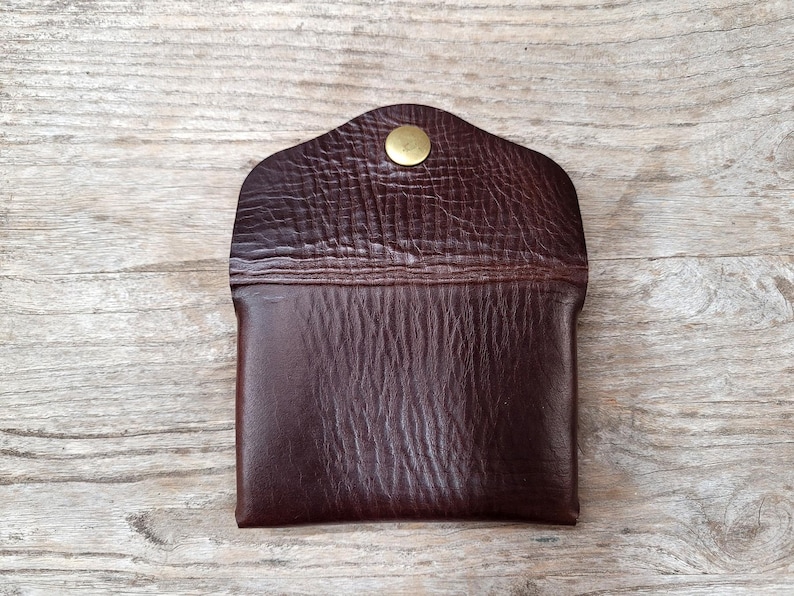 May include: A brown leather wallet with a gold button closure. The wallet has a textured surface and a flap that folds over the front.