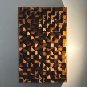 May include: A rectangular wooden wall art piece with a geometric design. The artwork features numerous small, angled wooden blocks in varying shades of brown, creating a textured, three-dimensional effect. The piece is framed in a darker wood.
