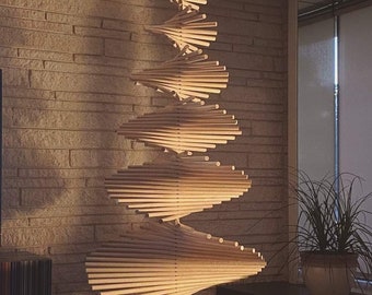 May include: A wooden Christmas tree sculpture made of thin, light brown wooden dowels arranged in a spiral pattern. The sculpture is hanging from the ceiling and is illuminated by sunlight.