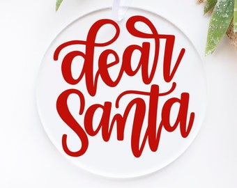 May include: White round ornament with a red cursive inscription that reads "dear santa".