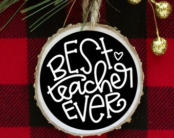May include: A round wooden ornament with a black background and white text that reads "BEST teacher EVER" with a small heart symbol. The ornament is hanging from a twine string.