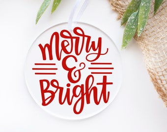 May include: Round white acrylic ornament with a red cursive inscription that reads "Merry & Bright".