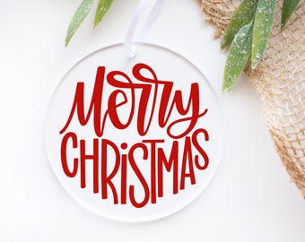 May include: Round, clear acrylic Christmas ornament with a red cursive inscription that reads "Merry Christmas".