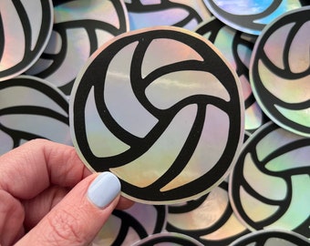 May include: A close-up of a stack of iridescent holographic stickers featuring a black and white volleyball design.
