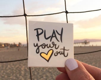 May include: A white card with the text "PLAY your heart out" in black lettering. A gold heart is in the middle of the text.
