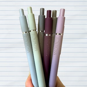 May include: Six pens with silver accents and the name "MACKENZIE" engraved on each. The pens are in shades of gray, light blue, green, purple, and lavender.