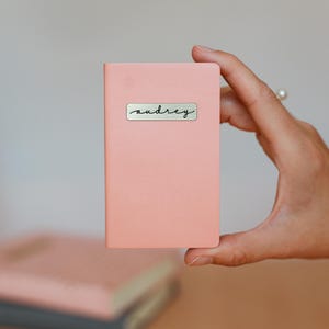 May include: A pink notebook with a gold sticker that says "audrey" on it.