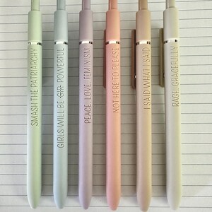 May include: Six pastel-colored pens with gold-colored clips and text. The pens are in shades of green, blue, purple, peach, tan, and white. The text on the pens includes phrases like "SMASH THE PATRIARCHY" and "RAGE, GRACEFULLY."