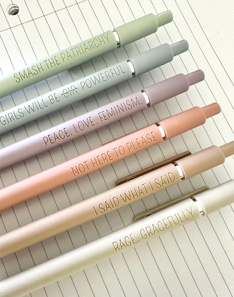 May include: Six pastel-colored pens with silver accents and matching caps. Each pen is engraved with a different empowering phrase: "SMASH THE PATRIARCHY," "GIRLS WILL BE GIR POWERFUL," "PEACE. LOVE. FEMINISM," "NOT HERE TO PLEASE," "I SAID WHAT I SAID," and "RAGE, GRACEFULLY."