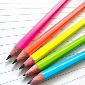 May include: Four colored pencils on a lined notebook. The pencils are pink, orange, yellow, and blue.