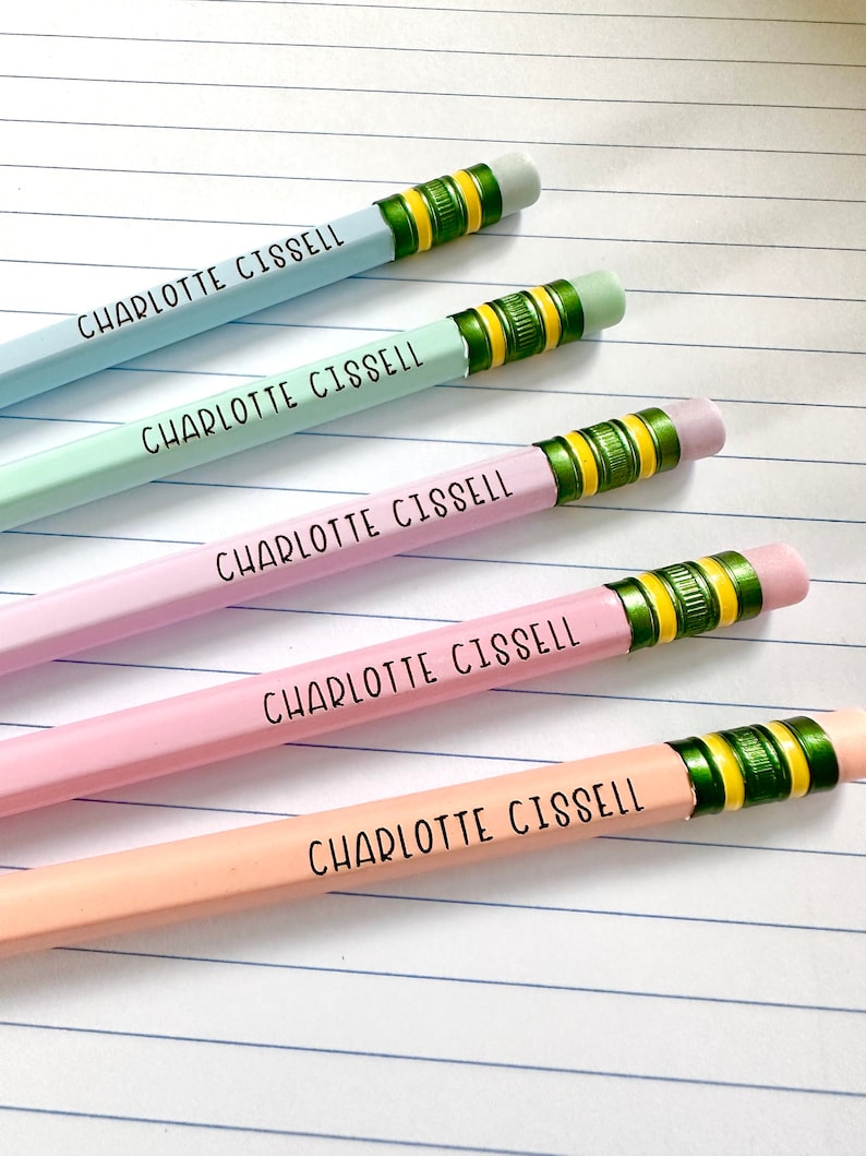 May include: Five personalized pencils with the name "Charlotte Cissell" printed on them. The pencils are in different pastel colors: blue, light blue, pink, and peach. Each pencil has a green and yellow eraser top.